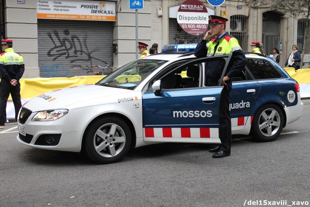 Un agente de los Mossos d'Esquadra habla por el móvil junto a un coche patrulla.